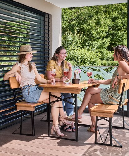 Friends sit together on the small beer garden table set Shorty with backrest and enjoy drinks on the terrace.