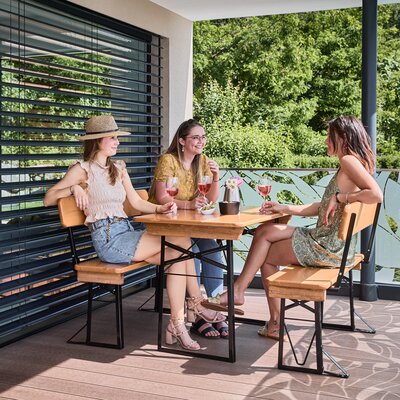 Friends sit together on the small beer garden table set Shorty with backrest and enjoy drinks on the terrace.