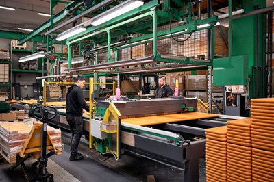 Two employees are working at a machine, preparing benches and tables for the next production step.