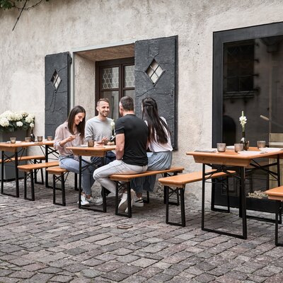 Four people are sitting on the small beer garden table set in the outdoor area of a restaurant.