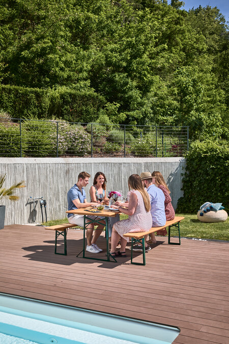 Five people enjoy the good weather on a wide beer garden table set in the garden.