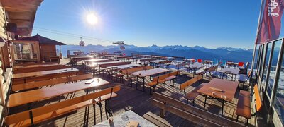 Breite Bierzeltgarnituren mit Lehne sind auf einer Alm vor einer Hütte im Winter aufgestellt.